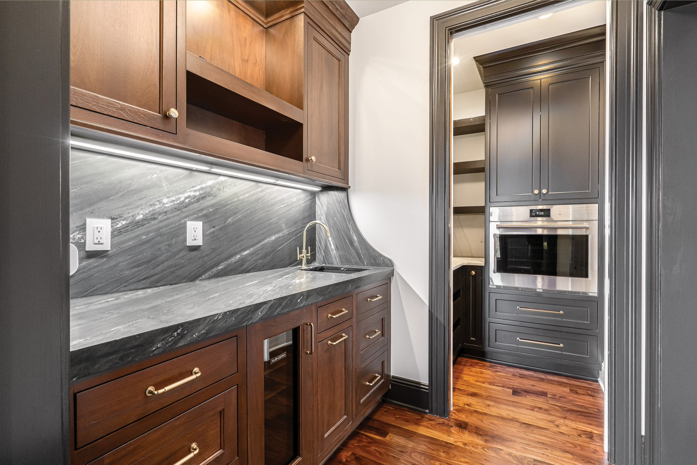Butler’s pantry with dark marble counters, walnut cabinetry and a wall oven