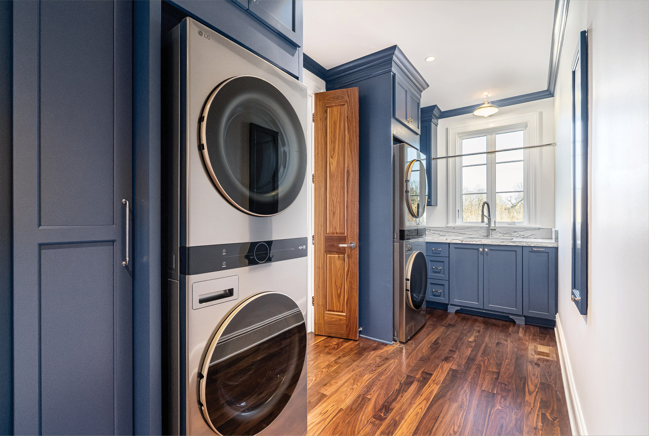 Laundry and mudroom in navy cabinetry with walnut floors and a marble counter
